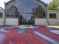 the building is white with a red swirl pattern and green trees in the background and a colorful paint on the floor is a rainbow