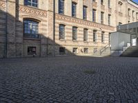 a brick courtyard in front of a very large building with stairs and steps leading to a second floor