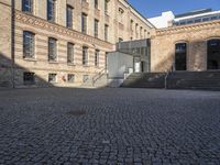 a brick courtyard in front of a very large building with stairs and steps leading to a second floor