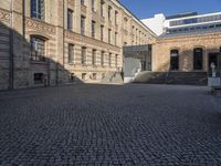 a brick courtyard in front of a very large building with stairs and steps leading to a second floor