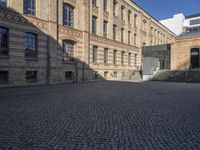 a brick courtyard in front of a very large building with stairs and steps leading to a second floor