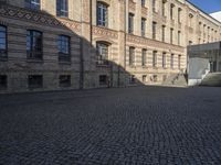 a brick courtyard in front of a very large building with stairs and steps leading to a second floor