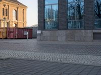 the building has multiple windows with many small red containers on them parked on the brick walkway