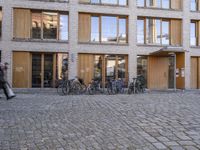 two people are walking and a row of bikes parked outside the building with many windows