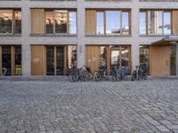 two people are walking and a row of bikes parked outside the building with many windows