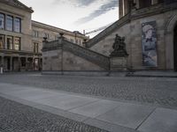 a picture of the building with statues is near people on the sidewalk and a dog sitting in the pavement