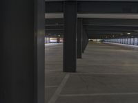 several black pillars are lined with windows in a large empty parking lot, with a woman walking in the distance