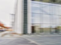 a blue scooter riding past an empty city street near a large building with windows