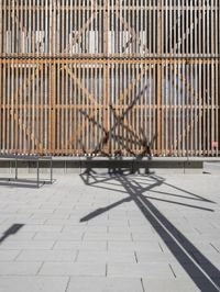 the sun is reflecting on the wall behind the fence and shadow from the bicycle on the street