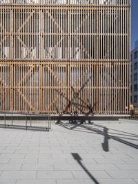 the sun is reflecting on the wall behind the fence and shadow from the bicycle on the street