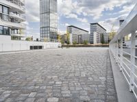 an urban courtyard area with cobblestone and modern buildings in the background by the water