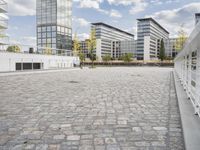 an urban courtyard area with cobblestone and modern buildings in the background by the water