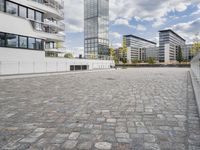 an urban courtyard area with cobblestone and modern buildings in the background by the water