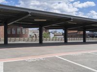 an empty parking lot with a row of benches and a metal roof overhang on a fence