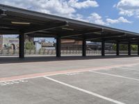 an empty parking lot with a row of benches and a metal roof overhang on a fence