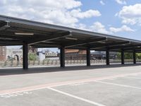 an empty parking lot with a row of benches and a metal roof overhang on a fence