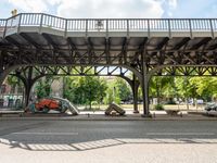 cars are sitting underneath an overpass on the side walk of a street with benches