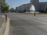 this is a picture of a park with fountains on the street and two people crossing