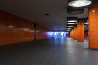 an empty subway corridor with several lights hanging from the ceiling and a single row of orange walls