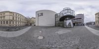 an image of a fish eye view of buildings and a bicycle rack, on the street