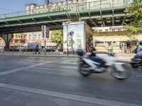 several people are riding motorcycles on a city street with green bridges overhangs over their heads