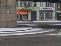 street in front of a building covered by snow with an umbrella on a snowy street with an overpass in the background