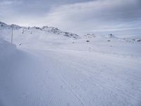 snow covered slope in the middle of a ski area as people ski on it near ski lift