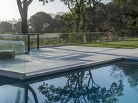 a glass box over looking a small pool surrounded by trees and greenery in the background