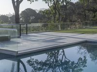 a glass box over looking a small pool surrounded by trees and greenery in the background