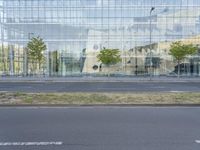 a glass building that is next to a street and trees on it's corner