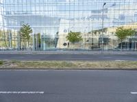 a glass building that is next to a street and trees on it's corner