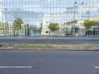 a glass building that is next to a street and trees on it's corner