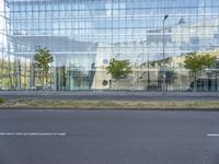 a glass building that is next to a street and trees on it's corner