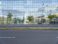 a glass building that is next to a street and trees on it's corner