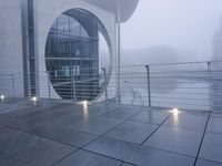 a glass building with an oval window on a foggy day in front of it