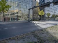 a glass building reflecting in another office building, a street is empty except for cars to pass