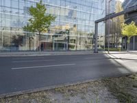 a glass building reflecting in another office building, a street is empty except for cars to pass