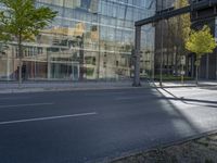 a glass building reflecting in another office building, a street is empty except for cars to pass