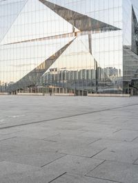 a man standing in front of a glass building with buildings in the background and an empty pavement below