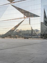 a man standing in front of a glass building with buildings in the background and an empty pavement below