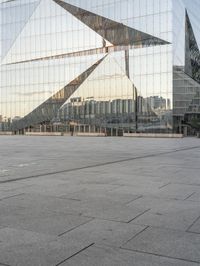 a man standing in front of a glass building with buildings in the background and an empty pavement below