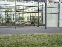 the building has glass walls and a sidewalk with green grass in it outside of it