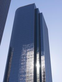 a tall glass building stands tall in front of a blue sky and some buildings with several windows