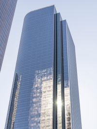 a tall glass building stands tall in front of a blue sky and some buildings with several windows