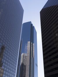 a tall glass building stands tall in front of a blue sky and some buildings with several windows