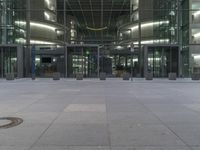 a man standing outside of a glass building in the evening, holding a backpack and a cellphone