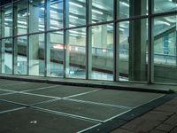 the glass building has a sidewalk and sidewalking area inside it at night with a person waiting