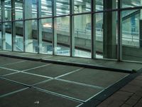 the glass building has a sidewalk and sidewalking area inside it at night with a person waiting