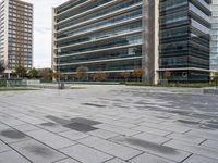 there is a big glass building next to the trees and benches in this empty city square