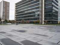 there is a big glass building next to the trees and benches in this empty city square